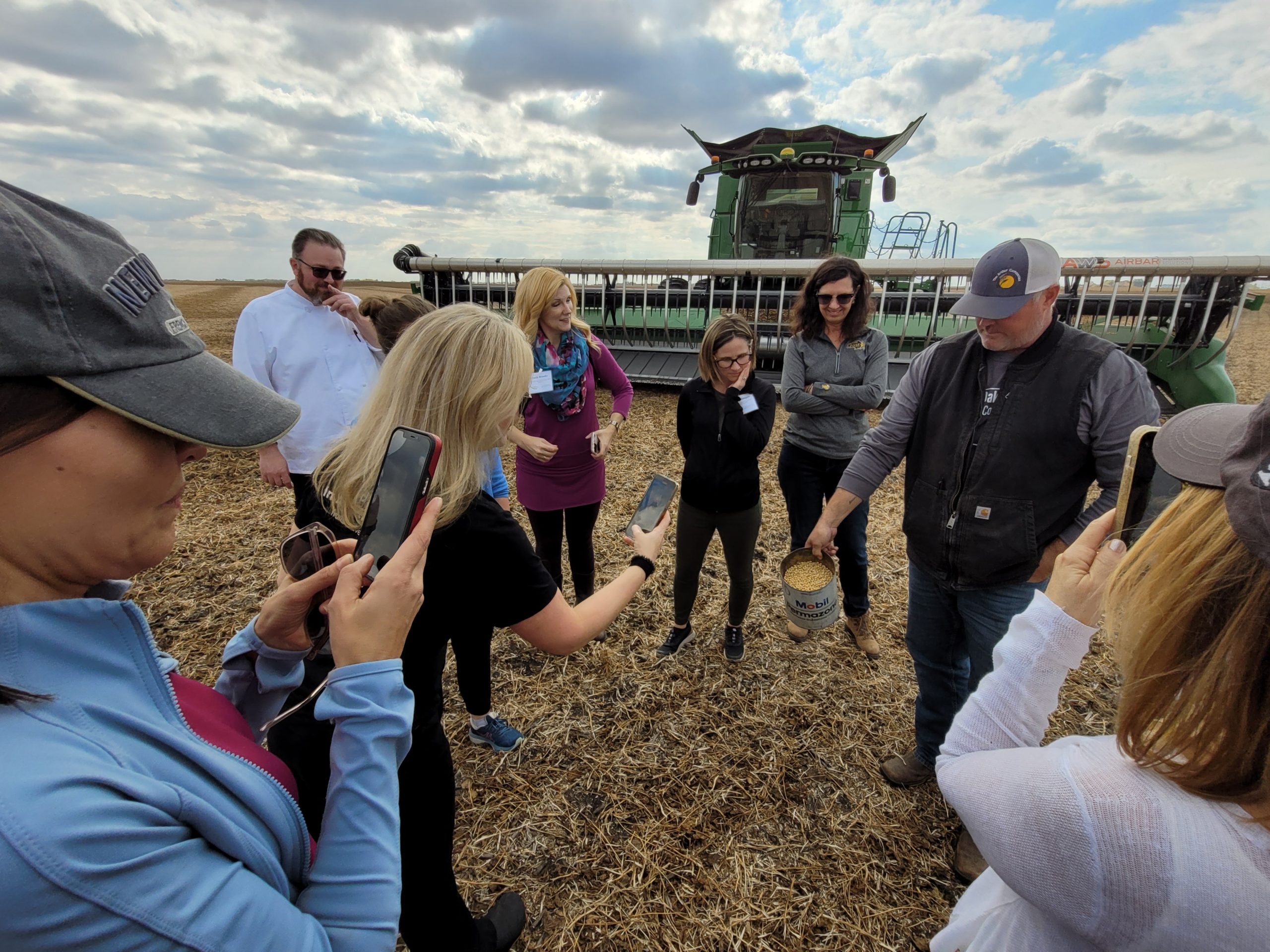 A ground of people with cell phones taking photos of harvested soybeans in a jug